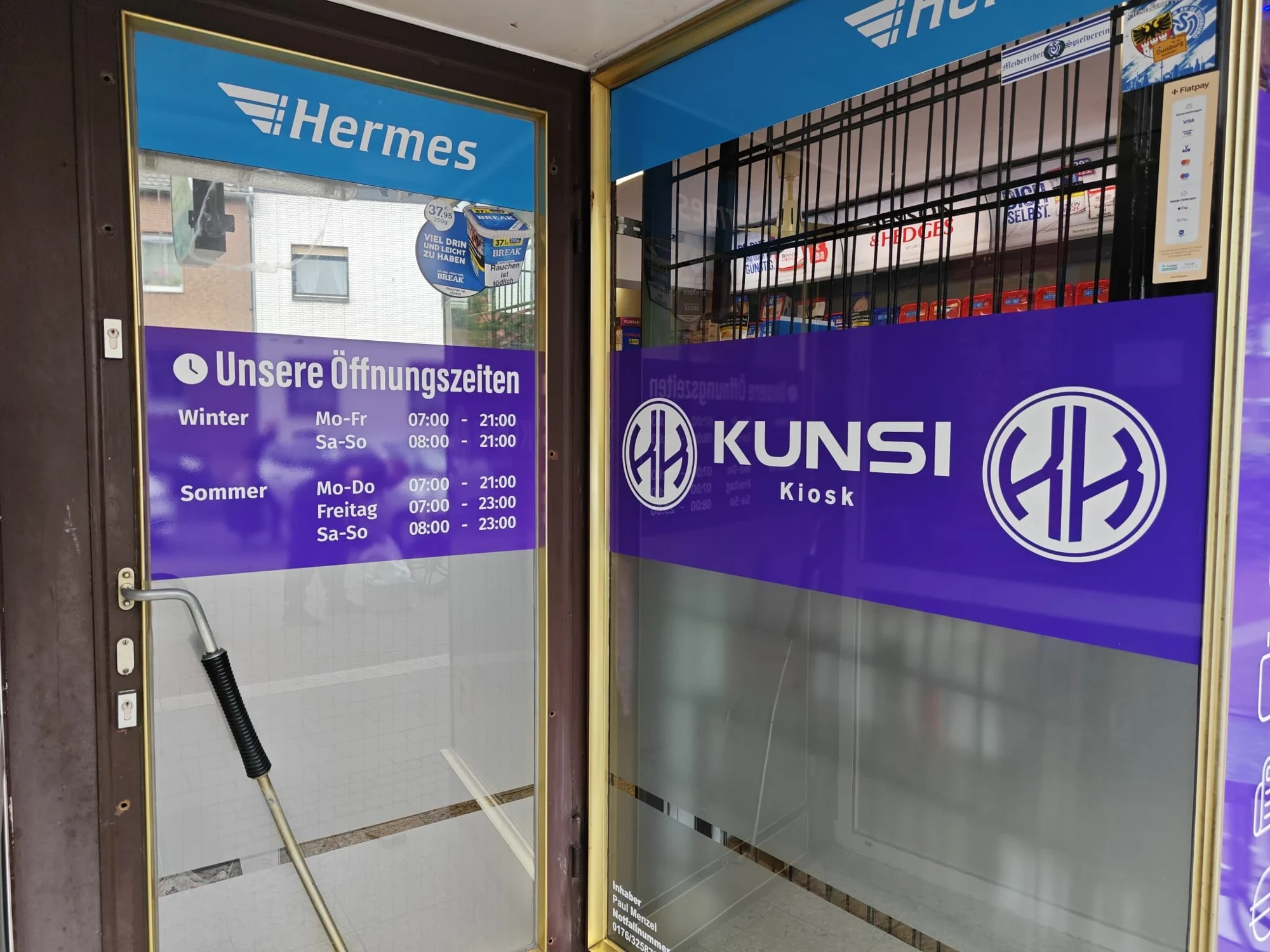 Weiße Öffnungszeiten und Beschriftung am Schaufenster eines Kiosks